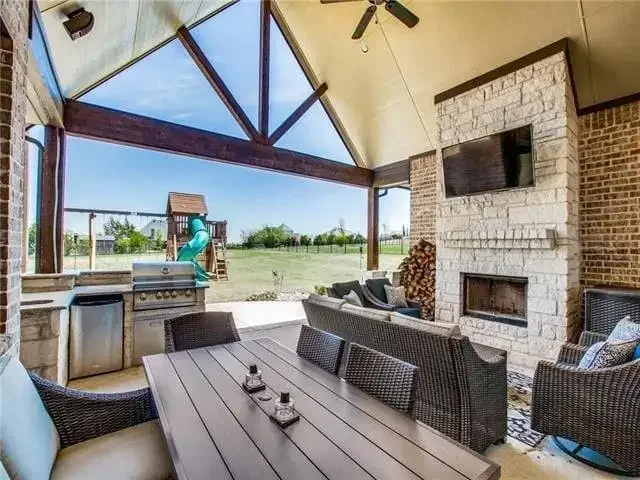 Covered outdoor living area with stone fireplace, built-in grill, and dining space